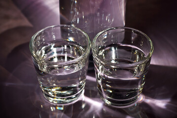 Glasses with alcohol near the bottle. Transparent drink on a purple background.