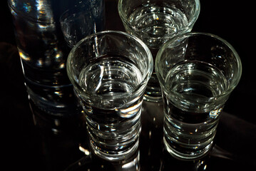 Glasses with alcohol near the bottle. Transparent drink on a black background.