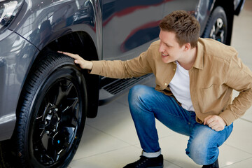 young caucasian man admires design of his new car in dealership, happy male enjoy perfectness of auto wheels