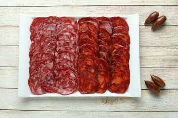 Serving of Iberian chorizo and salami garnished with acorns in rectangular plate on light wooden table