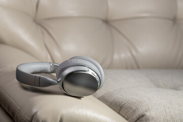 Bluetooth wireless headphones on  light, leather sofa. Modern devices for listening to music. Studio shot, copy space.