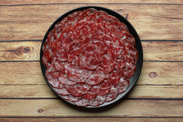 Ration of acorn-fed iberian sausage on black plate on rustic wooden table top view
