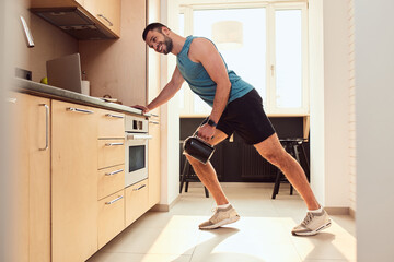 Cheerful young man doing exercise with electric kettle