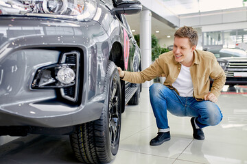 handsome caucasian guy checking, examining new car before making purchase in dealership. man look at auto and touch it