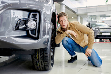 Handsome young man in casual wear checking wheels in a new car, surprised with it's perfection