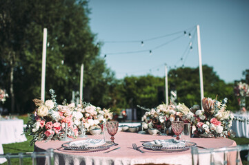 Presidium, table of the newlyweds. Floral arrangements of pink roses, anthurium, protea, eustoma, carnations, silver leaves. On the table is a pink velvet tablecloth. On the green lawn