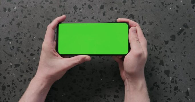 Top view man hands show smartphone with green screen on concrete background