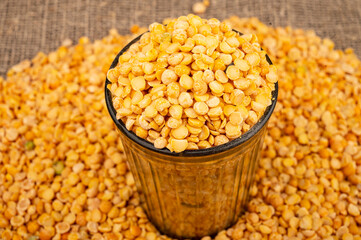 Yellow split peas in a cut glass and grits scattered on a background of coarse-textured burlap. Traditional cereals for making soups and porridge. Close up.