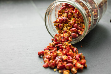 Wild rose hip dry fruit spilled on the black rock surface from glass jar