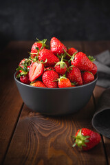 Heap of fresh strawberries in ceramic bowl  on wooden table with low key scene.