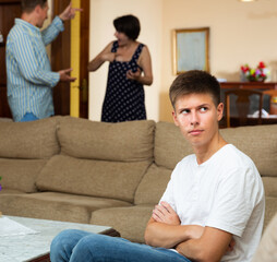 Parents swear among themselves. Offended son sits on a sofa