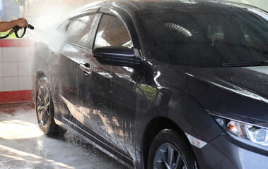 Closeup of grey car cleaning, washing with high pressure water spraying by male worker's hand. 