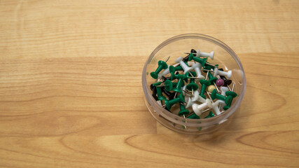 Obraz na płótnie Canvas Top view of full thumb tacks in a transparent box on wooden background. It is a short nail or pin used to fasten items to a wall or board for display. Selective focus on foreground.