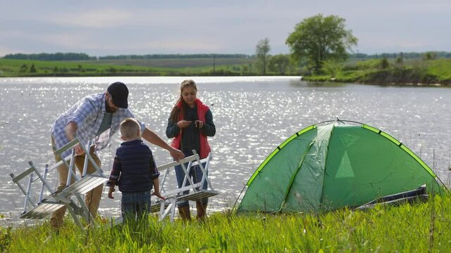 Dad and his son set up a folding table next to a tent in nature near the lake. Family on a picnic