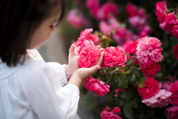 Cute little baby girl 3-4 year old holding pink roses in garden closeup. Summer season. Childhood.