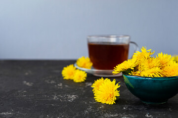 dandelion flowers and healthy tea on a black table. Blurred background. Summer breakfast and tea