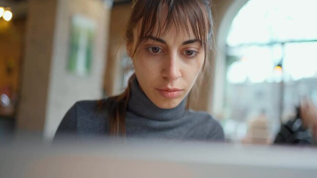 caucasian brunette woman looking at laptop screen while sitting workplace or cafe. Concept remote work, freelance, using laptop computer. right left pan camera movement