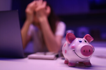 Piggy bank on table, an upset woman sits behind