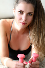 slender girl at home lies on carpet with dumbbells