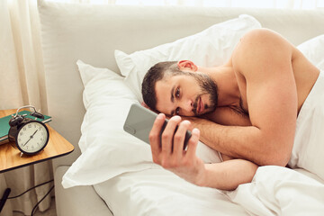 Attractive young man using cellphone in bedroom