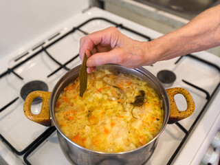Old woman is cooking vegetable soup on gas stove. Grandmother's wrinkled hand. Pan with homemade soup on gas stove.