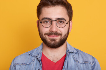 Indoor horizontal image of delighted good looking young man looking directly at camera, smiling...