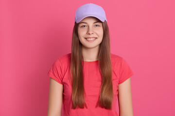 Shot of fit young woman wearing casual t shirt standing isolated over rosy background and looking at camera. Beautiful model in baseball cap with charming smile.