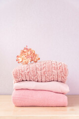 Fototapeta na wymiar Stack of winter or autumn womens clothes. Pile of colorful knitted cozy warm pink sweaters or pullover on wooden table.