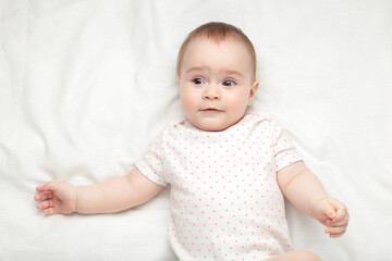 Cute baby girl lying and smile on white bed.