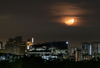 Big half moon shining over modern city buildings with some lights turned on