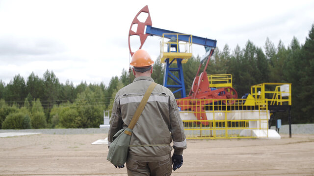 Follow Shot Oil Worker Walking To Oil Pump Jacks In Oil Field. Balancing Drive Rod Pumps Oil Rocker. Pumping Crude Oil For Fossil Fuel Energy With Drilling Rig In Oil Field.