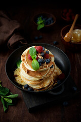 Pancakes decorated with raspberries, blueberries, mint and honey. Homemade fritters for breakfast in pan