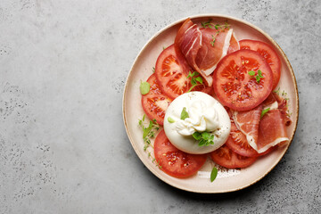 Buratta salad with tomatoes and prosciutto or jamon. Traditional Mediterranean appetizer. Italian Cuisine