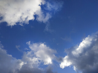 White and gray fluffy clouds illuminated by the sun on a blue sky background