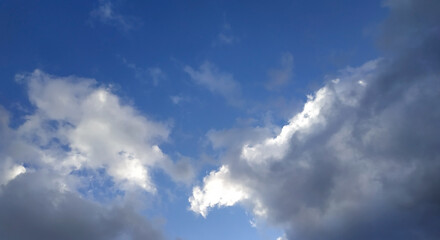 Obraz premium White and gray clouds illuminated by the sun on a blue sky background