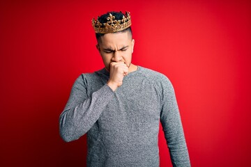 Young handsome man wearing golden crown of prince over isolated red background feeling unwell and...