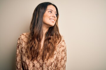 Young beautiful brunette woman wearing casual t-shirt standing over white background looking away to side with smile on face, natural expression. Laughing confident.