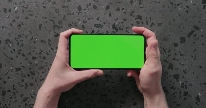 Top view man hands watch something on smartphone with green screen on concrete background