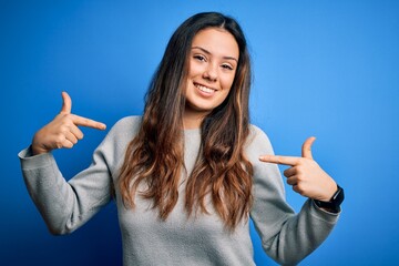 Young beautiful brunette woman wearing casual sweater standing over blue background looking...