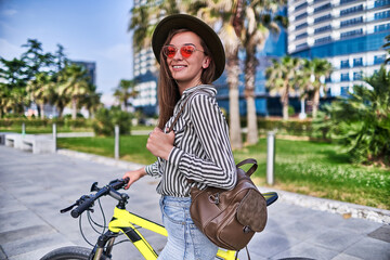 Stylish smiling modern brunette young hipster woman in a fashionable outfit wearing felt hat and...