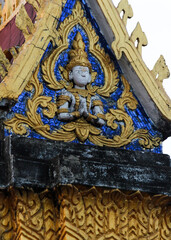 Fototapeta na wymiar Golden fresco of a buddha image on a blue glass mosaic design on a gable of a wat or buddhist temple in Siamese Lao PDR, Southeast Asia