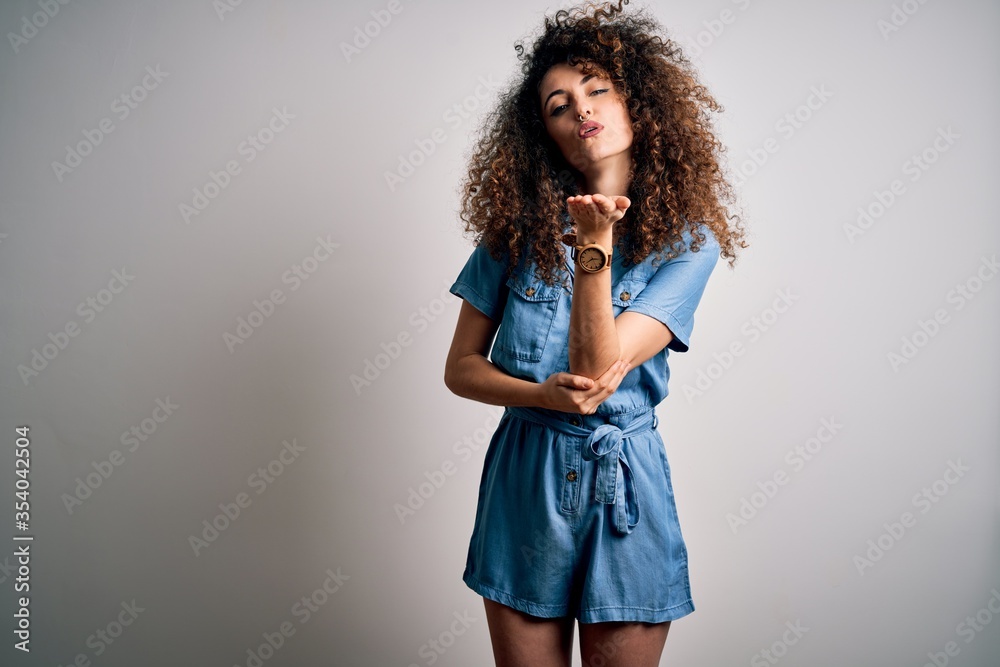 Wall mural young beautiful woman with curly hair and piercing wearing casual denim dress looking at the camera 