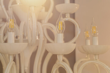 Close up on crystal of classic style chandelier, is a branched ornamental light fixture designed to be mounted on ceilings. Soft warm filter, selective focus. Indoor. White light glass.