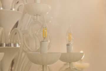 Close up on crystal of classic style chandelier, is a branched ornamental light fixture designed to be mounted on ceilings. Soft warm filter, selective focus. White glossy glass.