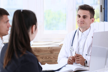 Male family doctor listen carefully young couple in office