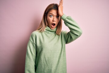 Young beautiful blonde woman wearing winter wool sweater over pink isolated background surprised with hand on head for mistake, remember error. Forgot, bad memory concept.