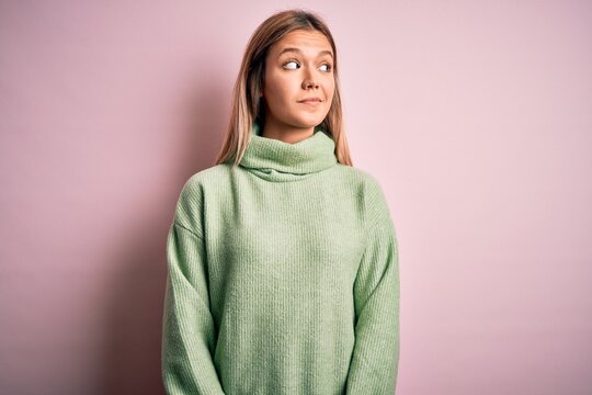 Young beautiful blonde woman wearing winter wool sweater over pink isolated background smiling looking to the side and staring away thinking.