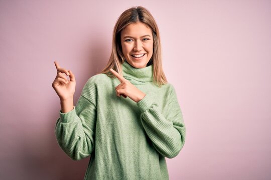 Young beautiful blonde woman wearing winter wool sweater over pink isolated background smiling and looking at the camera pointing with two hands and fingers to the side.