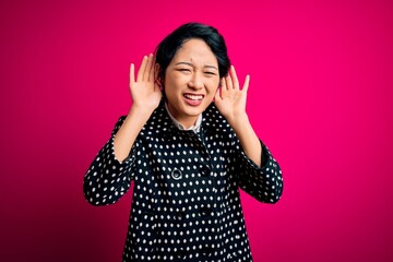 Young beautiful asian girl wearing casual jacket standing over isolated pink background Trying to hear both hands on ear gesture, curious for gossip. Hearing problem, deaf