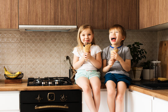 Two Little Kids Eating Ice Cream In Kitchen At Home